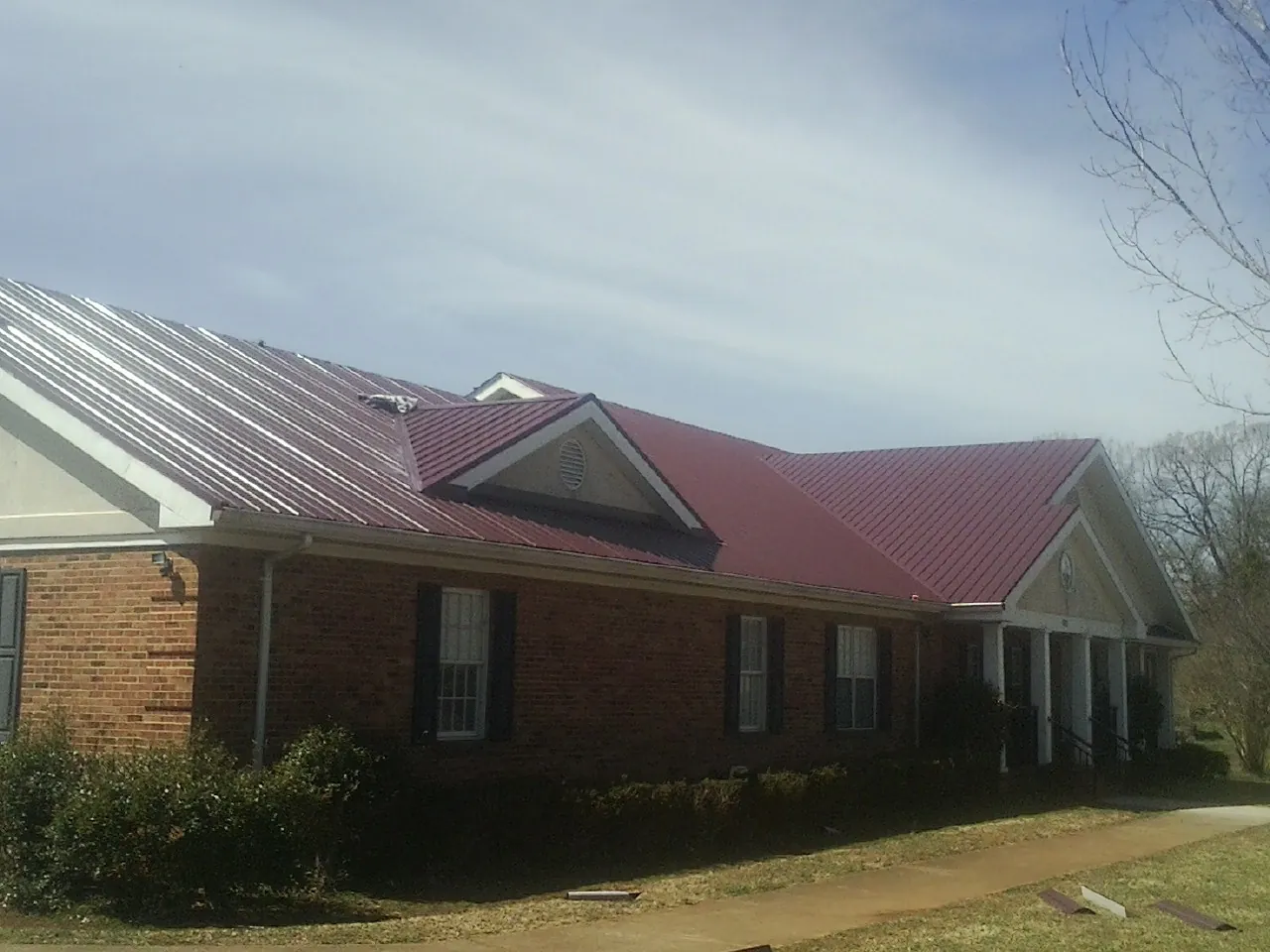 Red metal roof with gabled entries on a long brick building, from a Hail Damage Roof Repair job in Port William