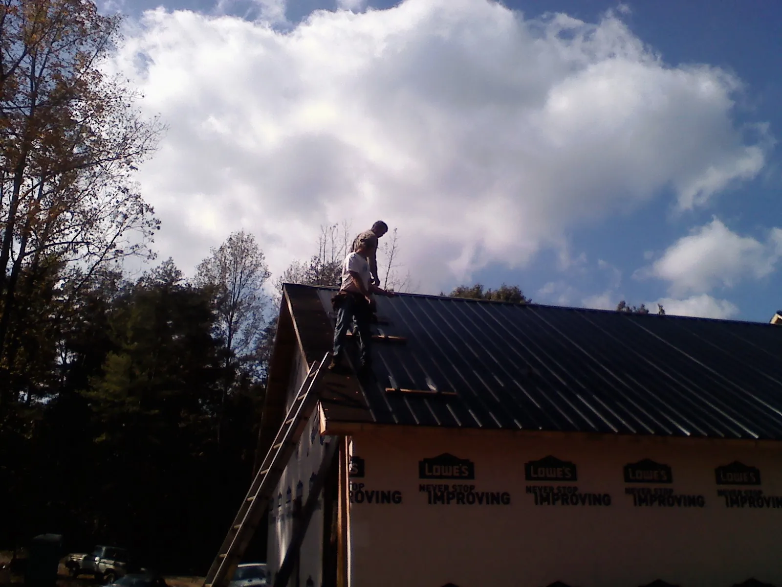 Roofer fastening dark metal panels high against a cloudy sky, from a Roof Inspection job in Port William