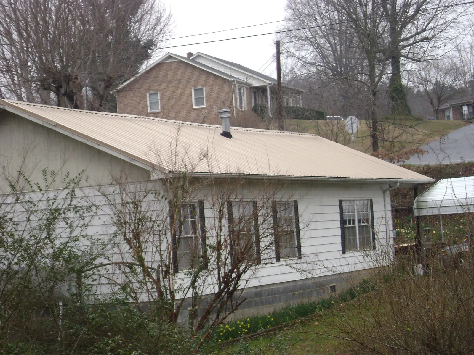 Tan metal roof on a white sided house set into a hillside — Commercial Roofing by Roofing Brothers in Port William